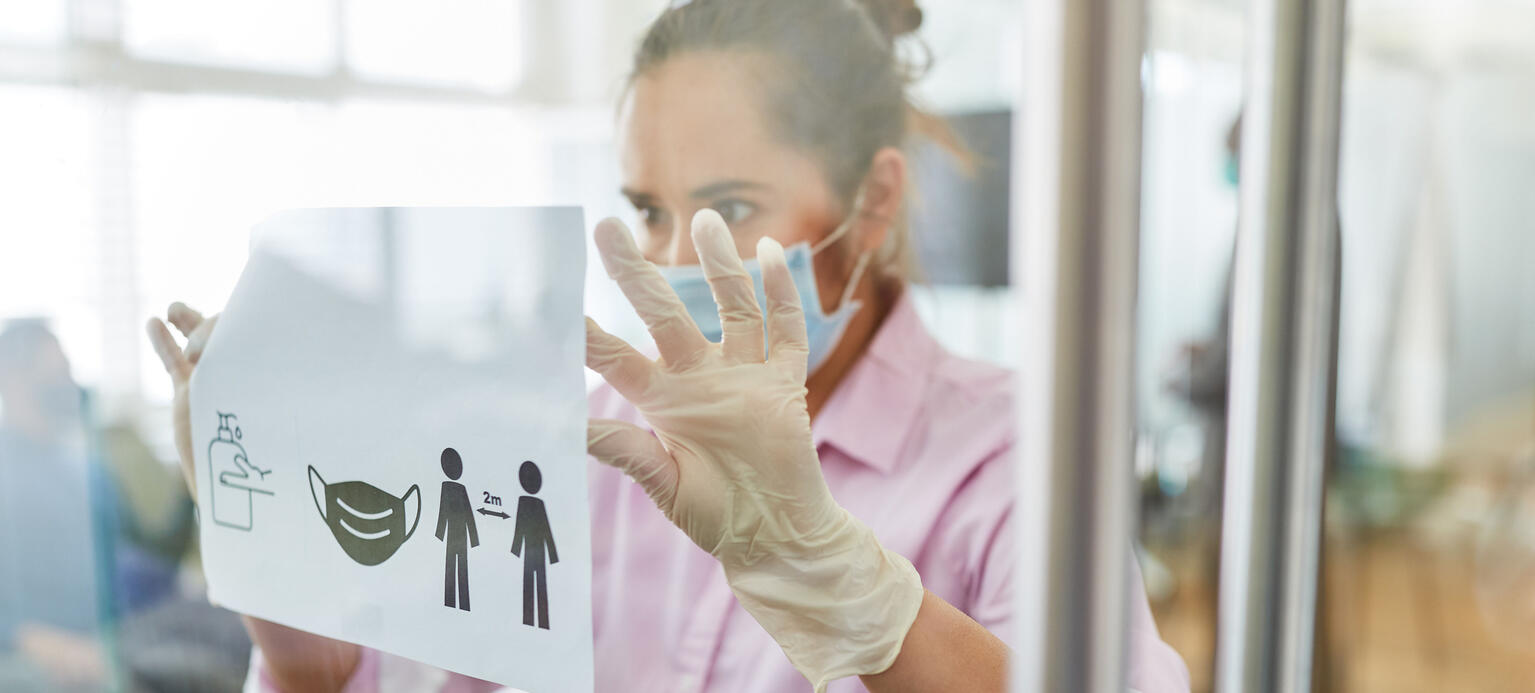 Business Frau befestigt Aushang mit Hygieneregeln für den Arbeitsplatz wegen Covid-19 