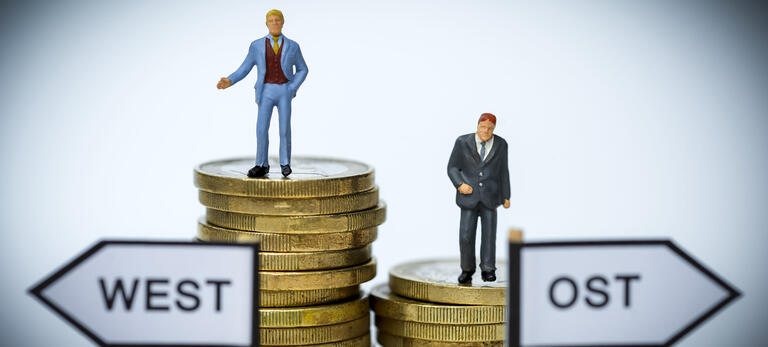 Geschäftsmänner-Miniaturfiguren auf Münzstapeln, ungleiche Gehälter in West- und Ostdeutschland
